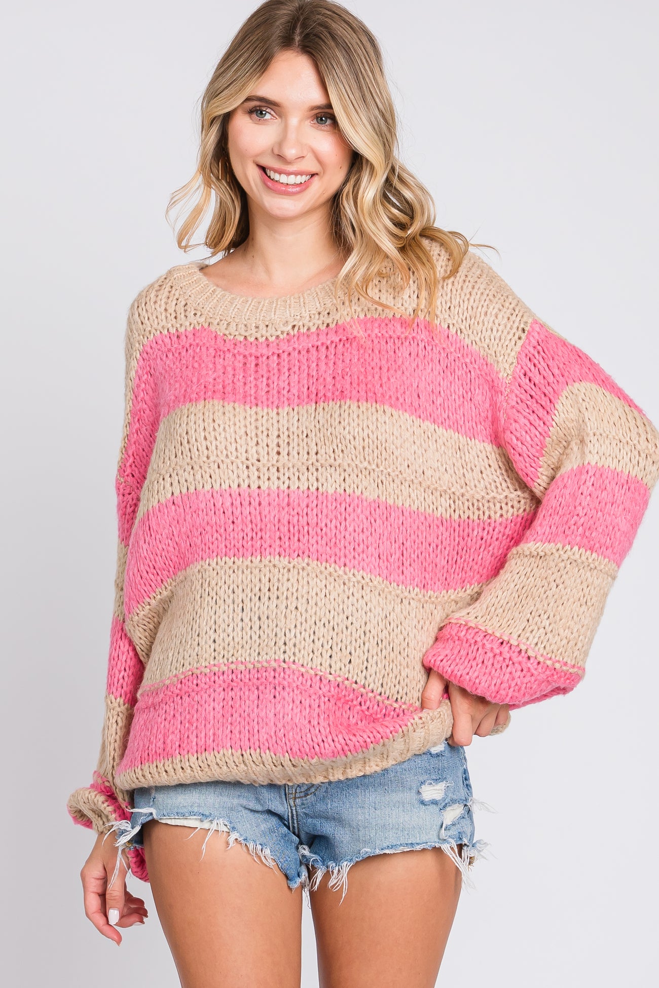 woman wearing a beige and pink striped oversized sweater paired with denim shorts