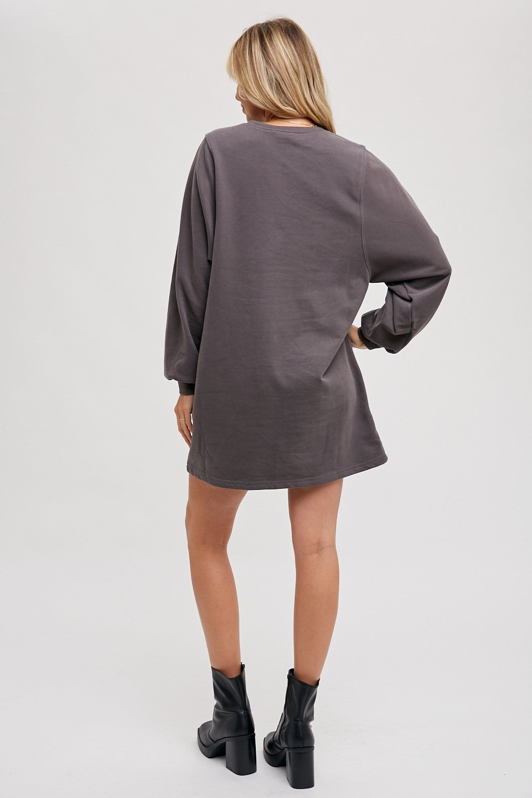 woman wearing a gray oversized sweatshirt dress with long sleeves and a relaxed fit, standing with her back to the camera