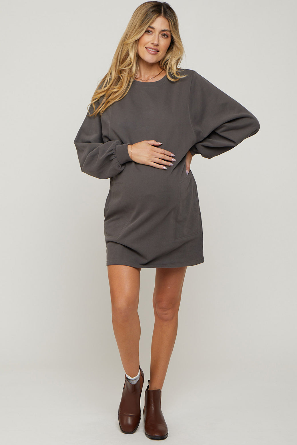 woman wearing a dark gray maternity sweatshirt dress and holding her baby bump