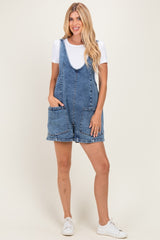 woman wearing a blue denim overall dress with large front pockets and paired with a white short sleeve top