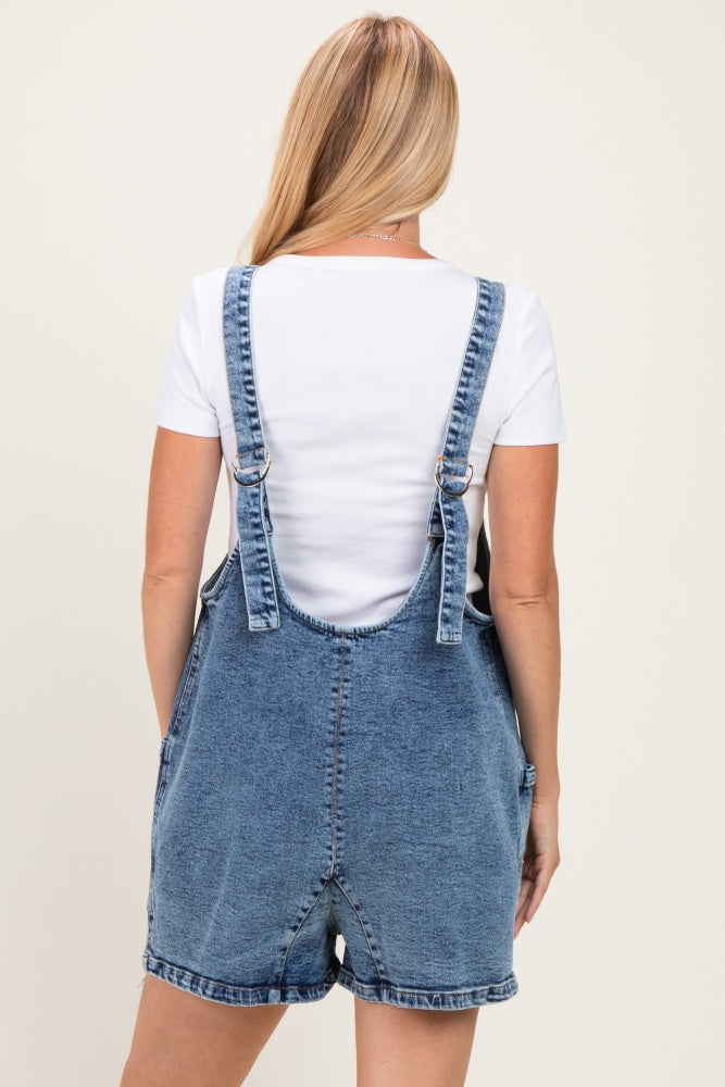 woman wearing a white short sleeve top under a blue denim overall dress, viewed from the back