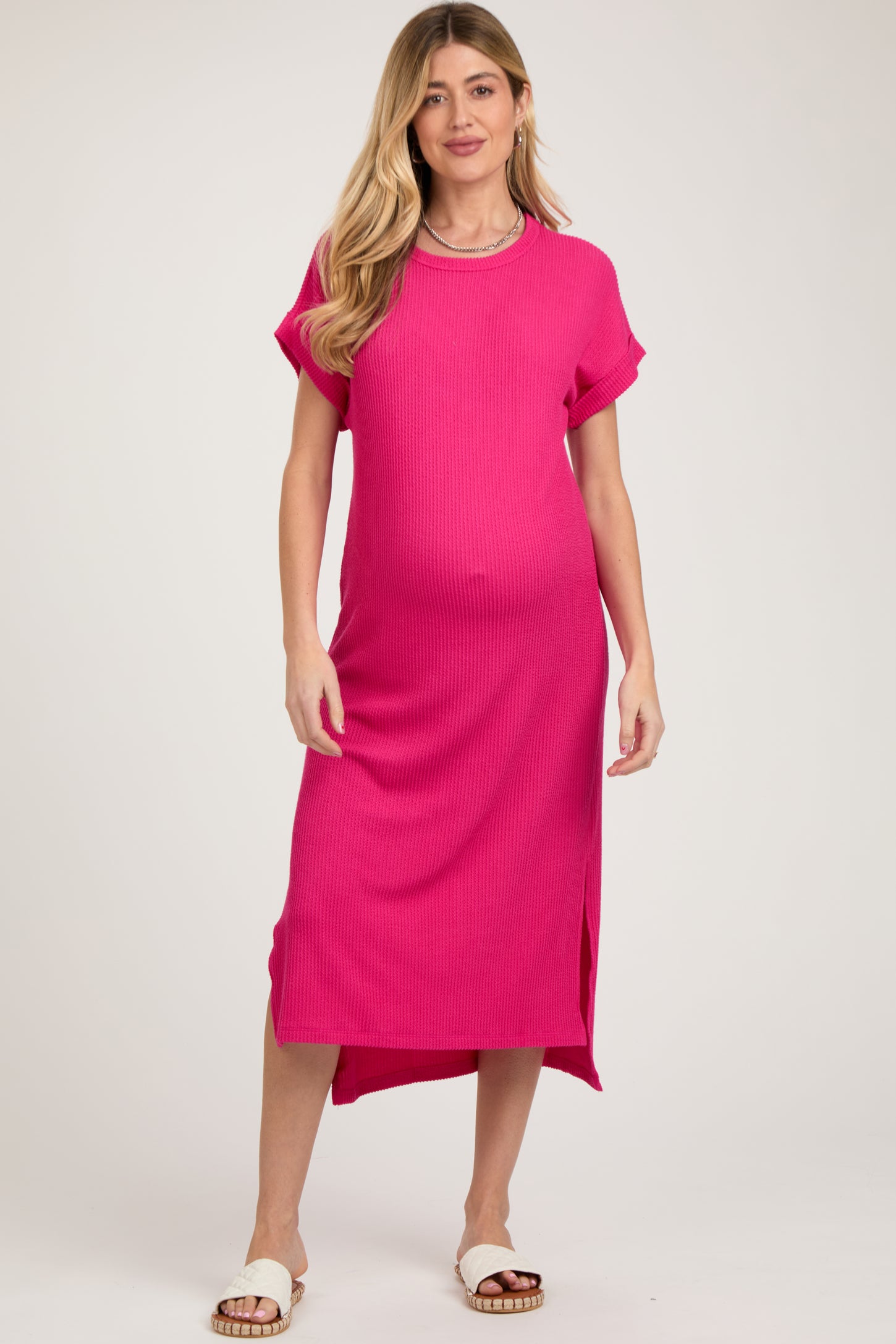 woman wearing a bright pink ribbed maternity dress with short sleeves and a side slit, showcasing her baby bump