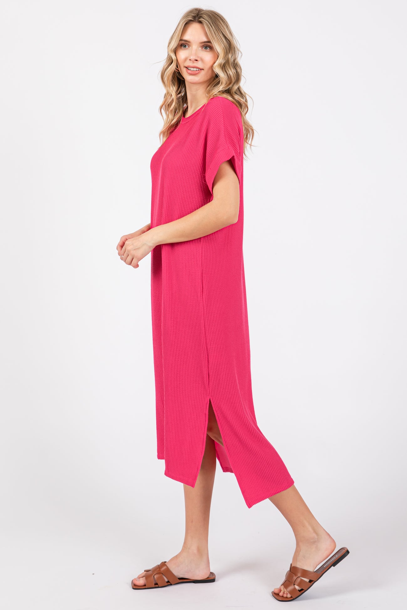 woman wearing a hot pink ribbed midi dress with side slits and short sleeves, standing in profile