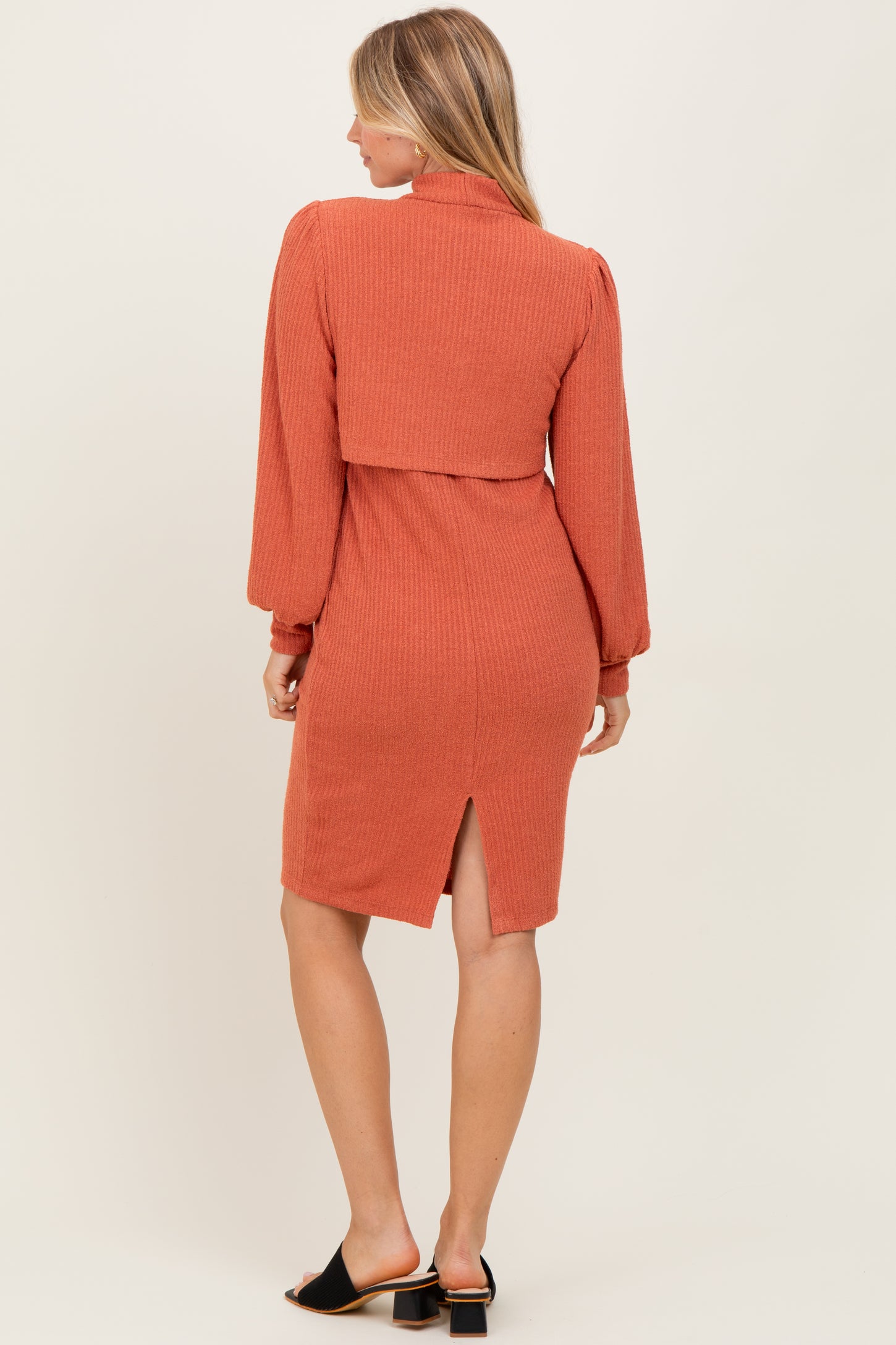 woman wearing a rust-colored ribbed midi dress with long sleeves and a back slit detail