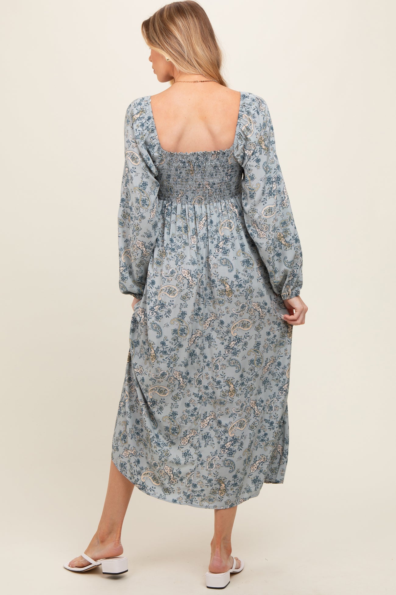 woman wearing a light blue floral print maternity dress with smocked bodice and long sleeves, showing her back