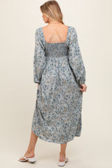 woman wearing a light blue floral print maternity dress with smocked bodice and long sleeves, showing her back