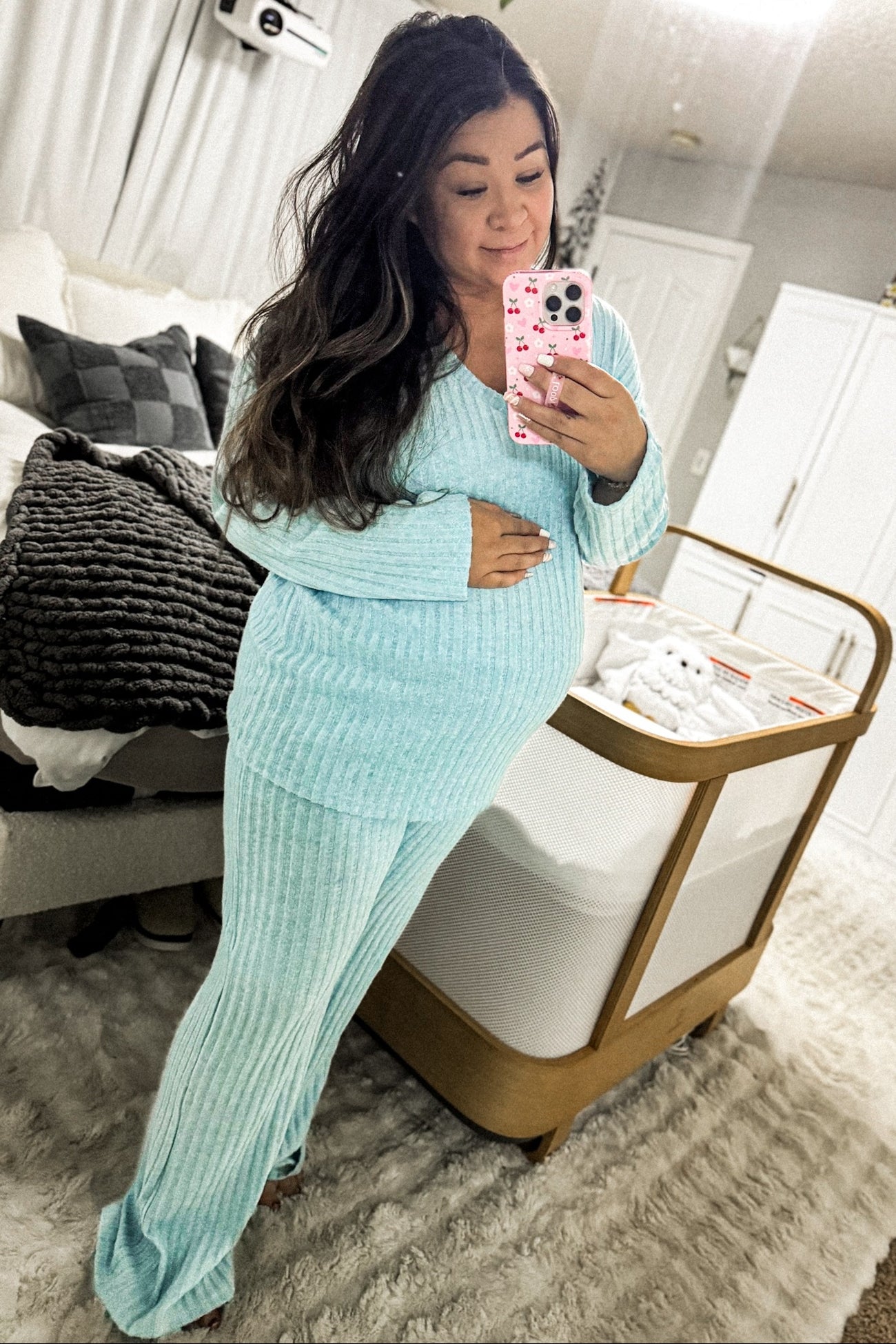 woman wearing a light blue maternity loungewear set, gently cradling her baby bump in a cozy bedroom setting
