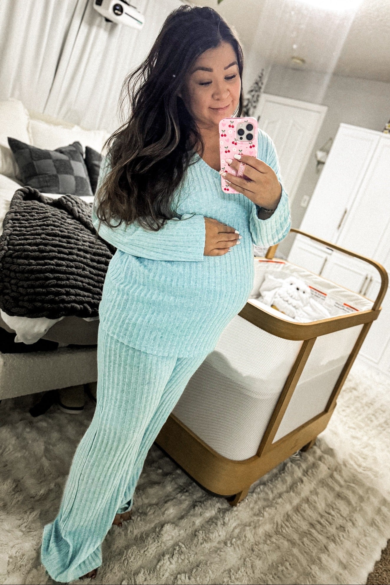woman wearing a light blue maternity loungewear set, gently cradling her baby bump in a cozy bedroom setting