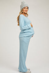 woman wearing a light blue ribbed maternity sweater and matching pants, gently cradling her baby bump