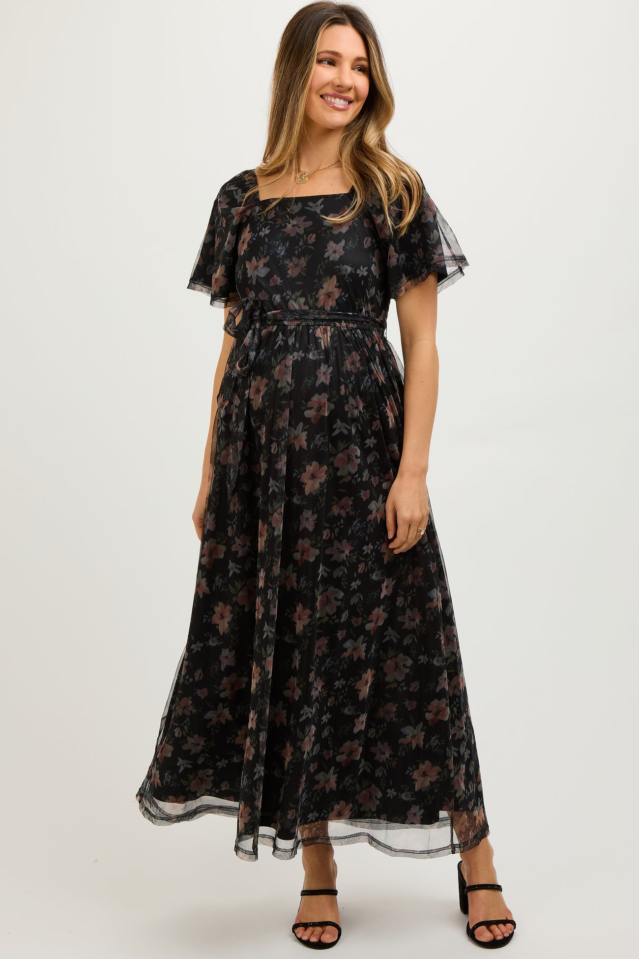 woman wearing a black floral maternity maxi dress with short flutter sleeves and a tie waist, showcasing her baby bump