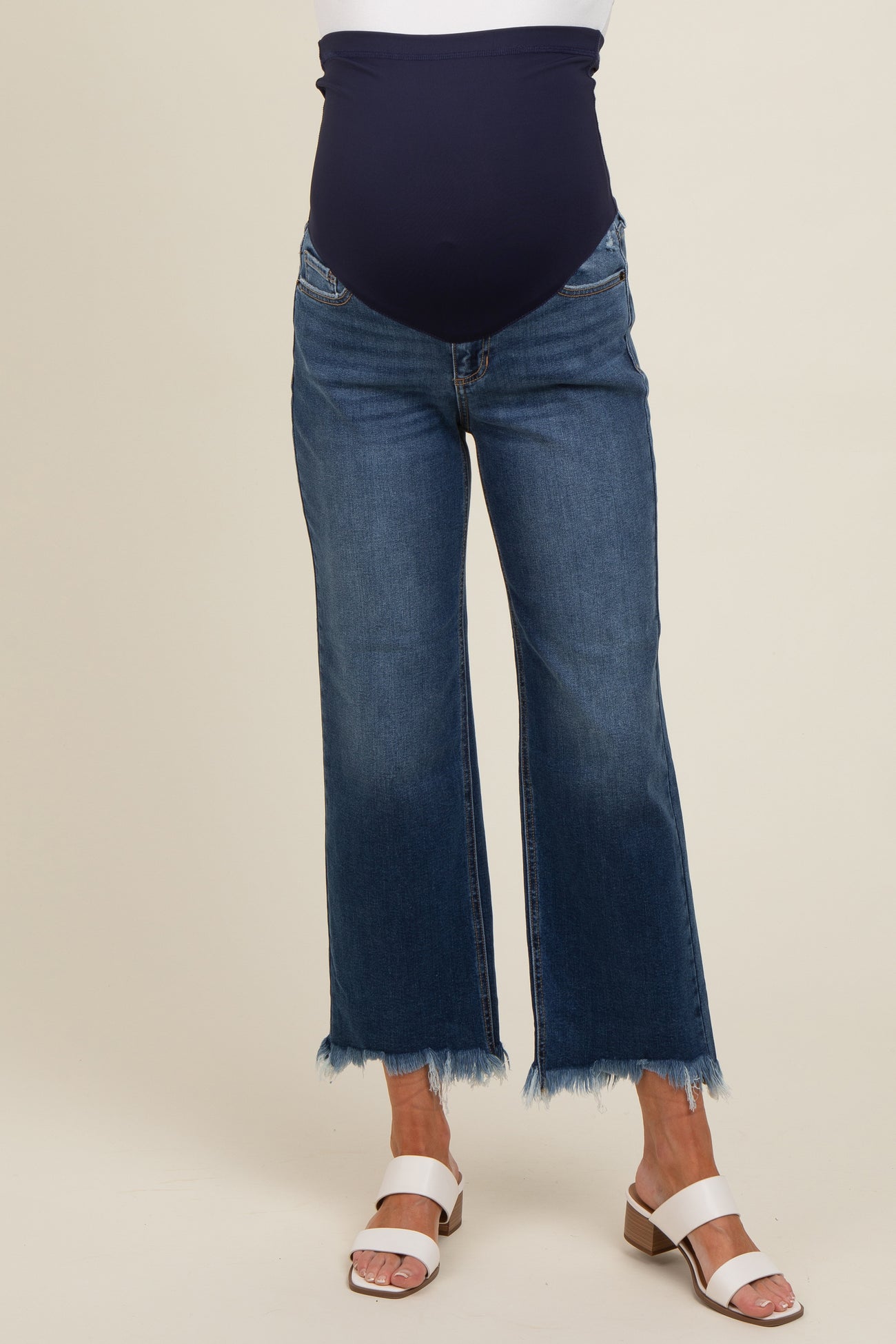 woman wearing dark blue maternity jeans with a stretchy belly panel and frayed hem, paired with white sandals