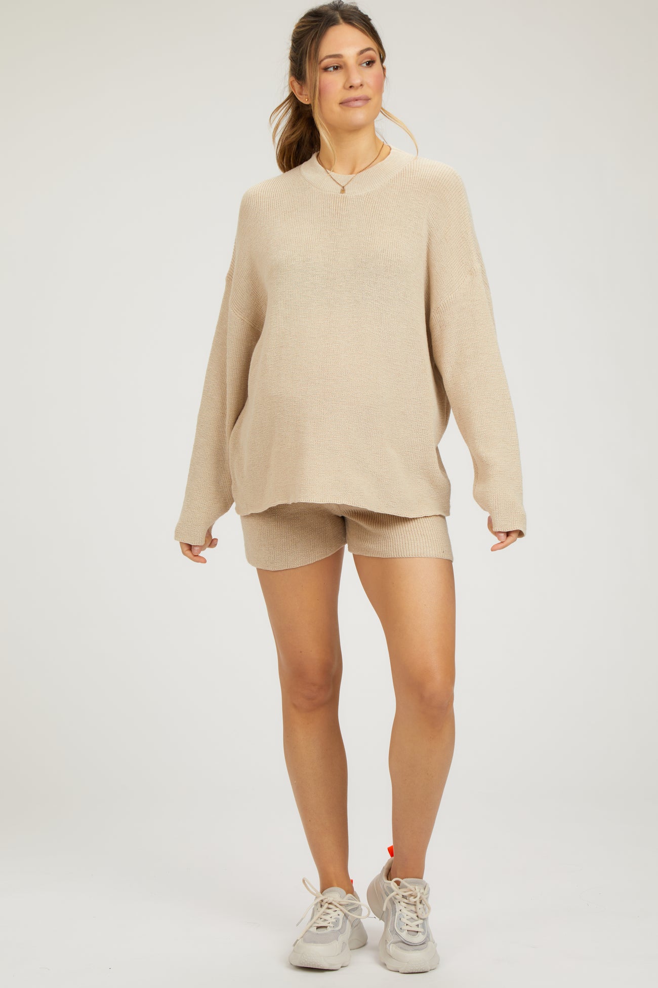 woman wearing a beige maternity oversized sweater and matching shorts with a visible baby bump