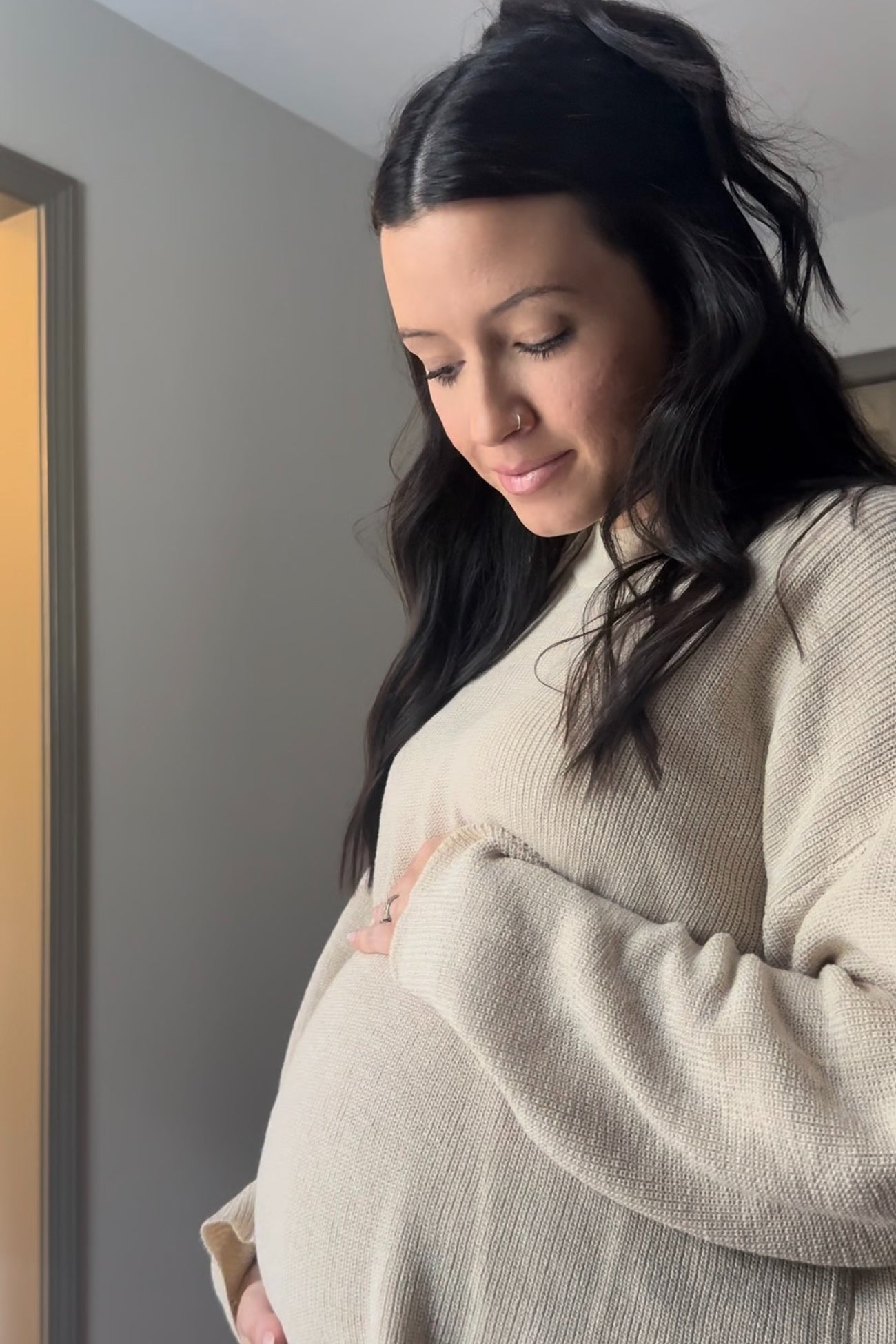woman wearing a beige long sleeve maternity sweater and holding her baby bump