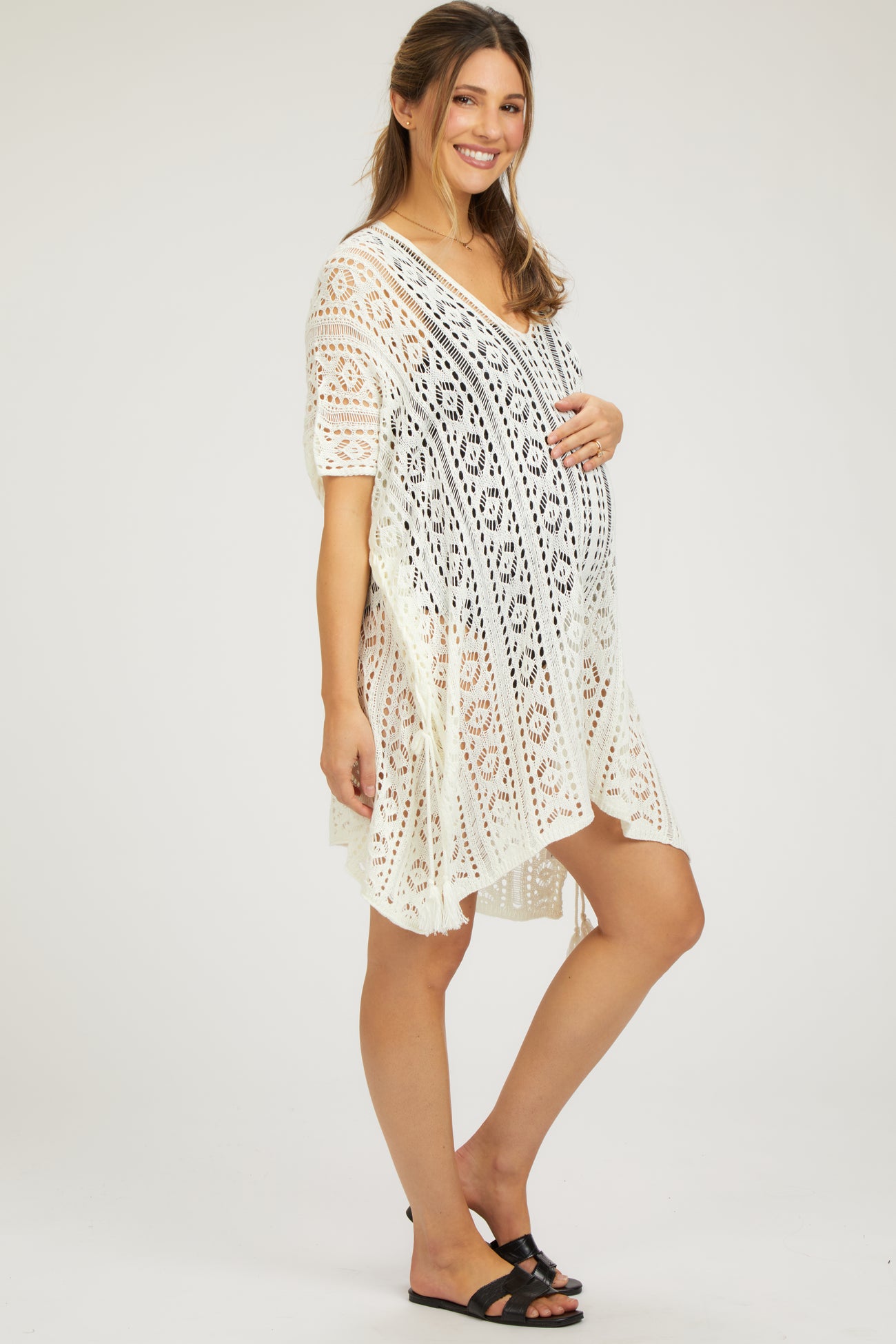 woman wearing a white lace maternity cover-up dress and holding her baby bump