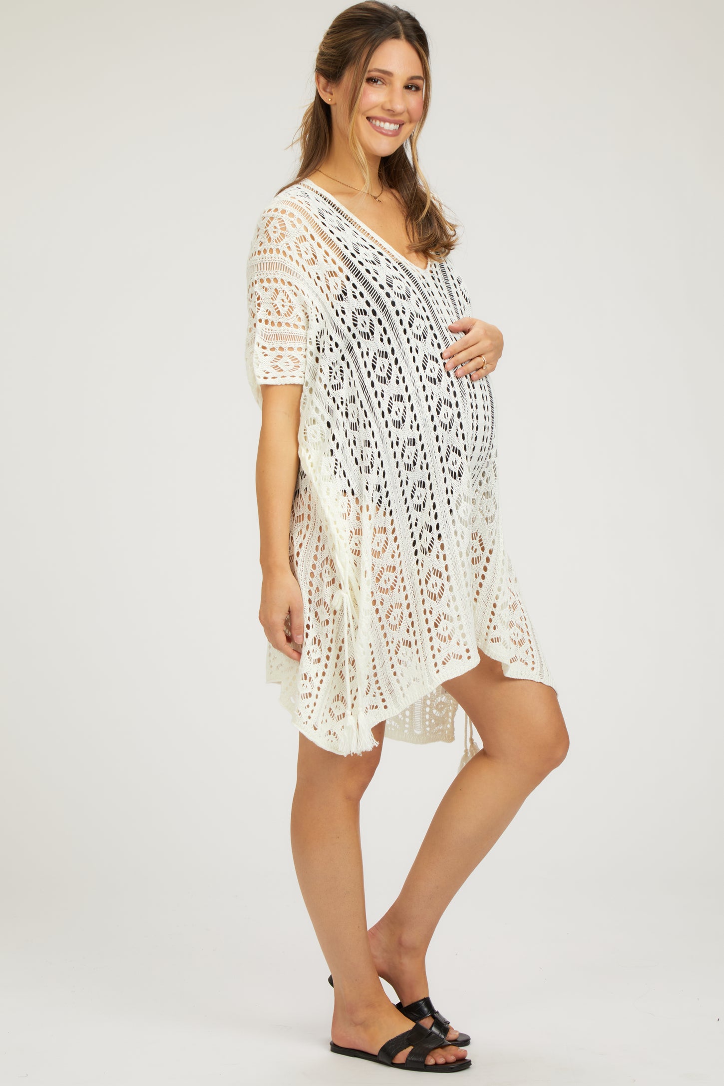 woman wearing a white lace maternity cover-up dress and holding her baby bump