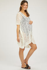 woman wearing a white lace maternity cover-up dress and holding her baby bump