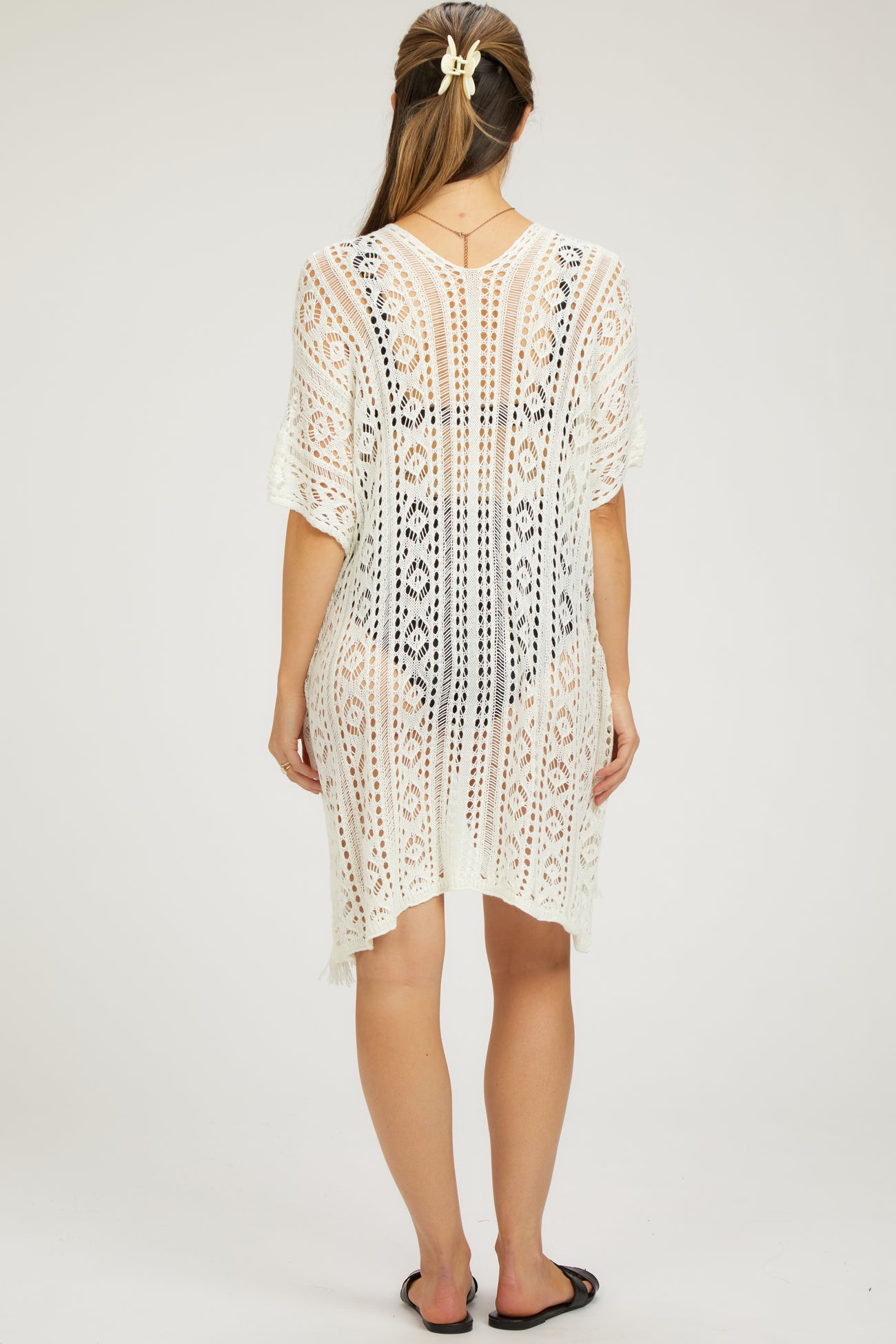 woman wearing a white crochet maternity cover-up with a loose fit and fringe details, showing a side view