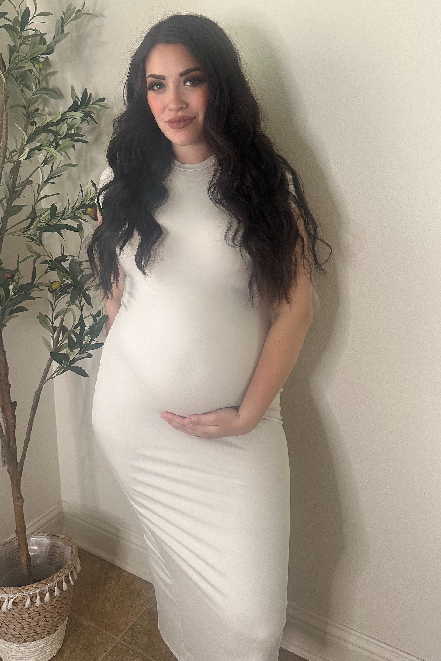 woman wearing a form-fitting white maternity dress and gently cradling her baby bump.