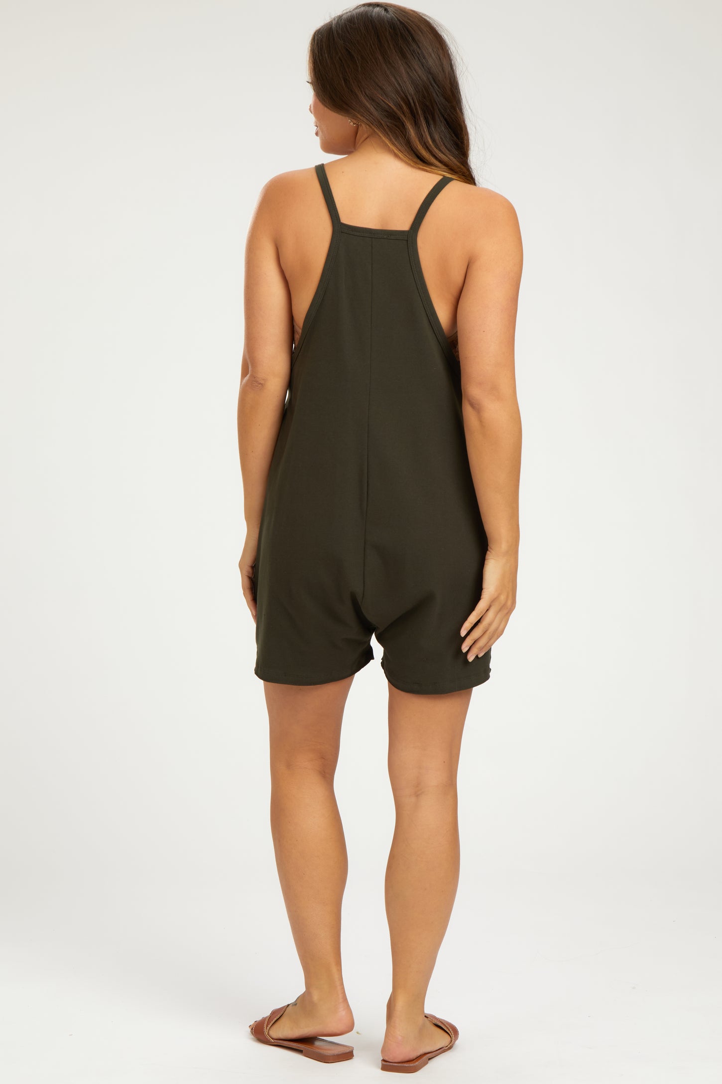woman wearing a dark green maternity romper with adjustable straps and a relaxed fit, showing a side view