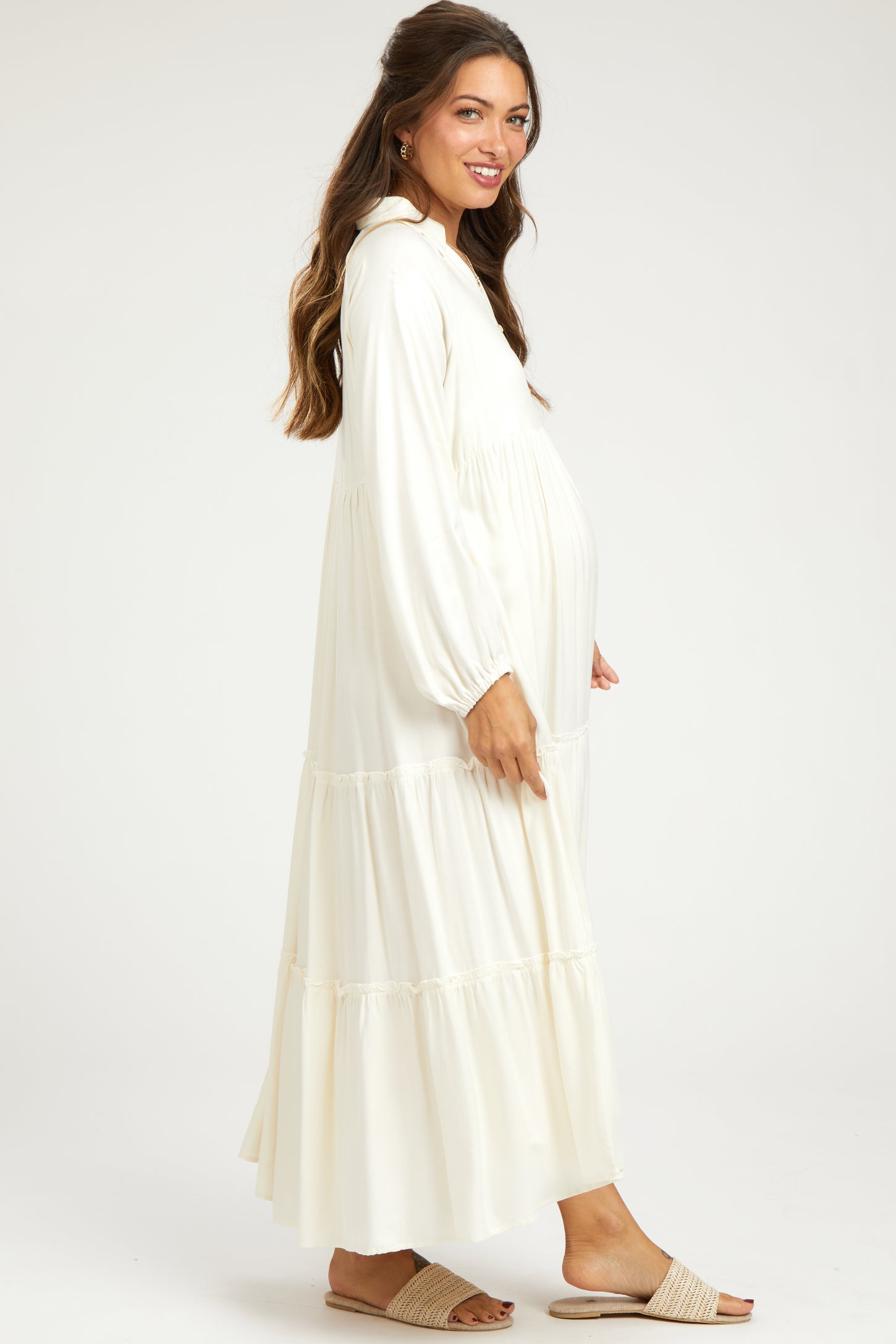 woman wearing a white maternity maxi dress with long sleeves and tiered details, showing her baby bump
