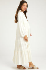 woman wearing a white maternity maxi dress with long sleeves and tiered details, showing her baby bump