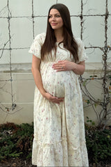 woman wearing a floral cream maternity dress and holding her baby bump while standing outdoors