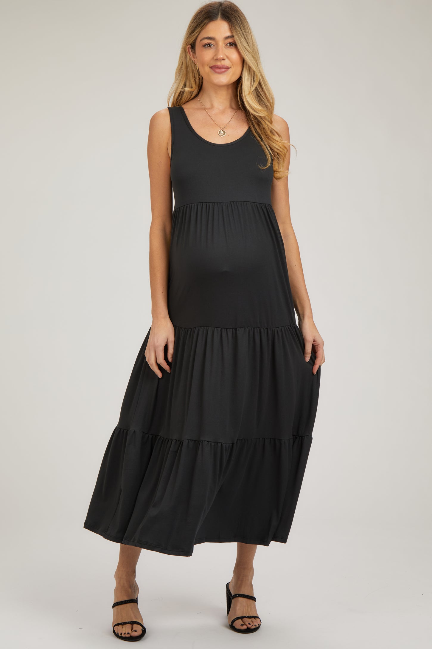woman wearing a black sleeveless tiered maternity maxi dress and showing her baby bump