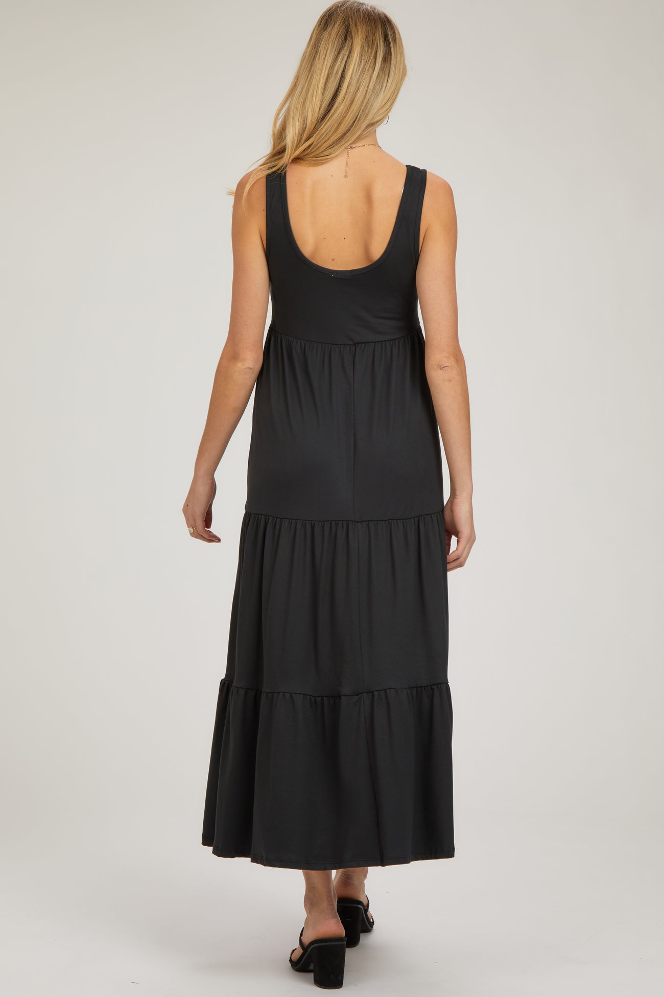woman wearing a black maternity maxi dress with a tiered skirt, showing the back view and a relaxed fit