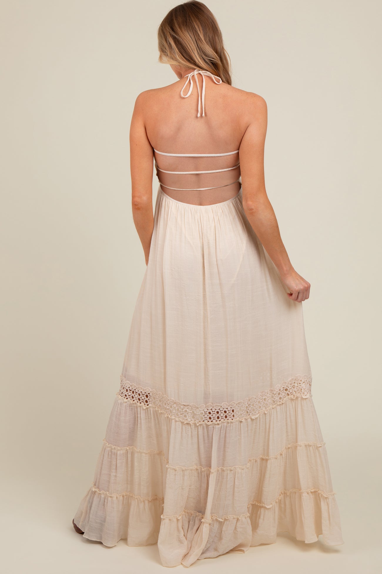 woman wearing a cream-colored maternity maxi dress with a halter neck and tiered ruffle details on the skirt