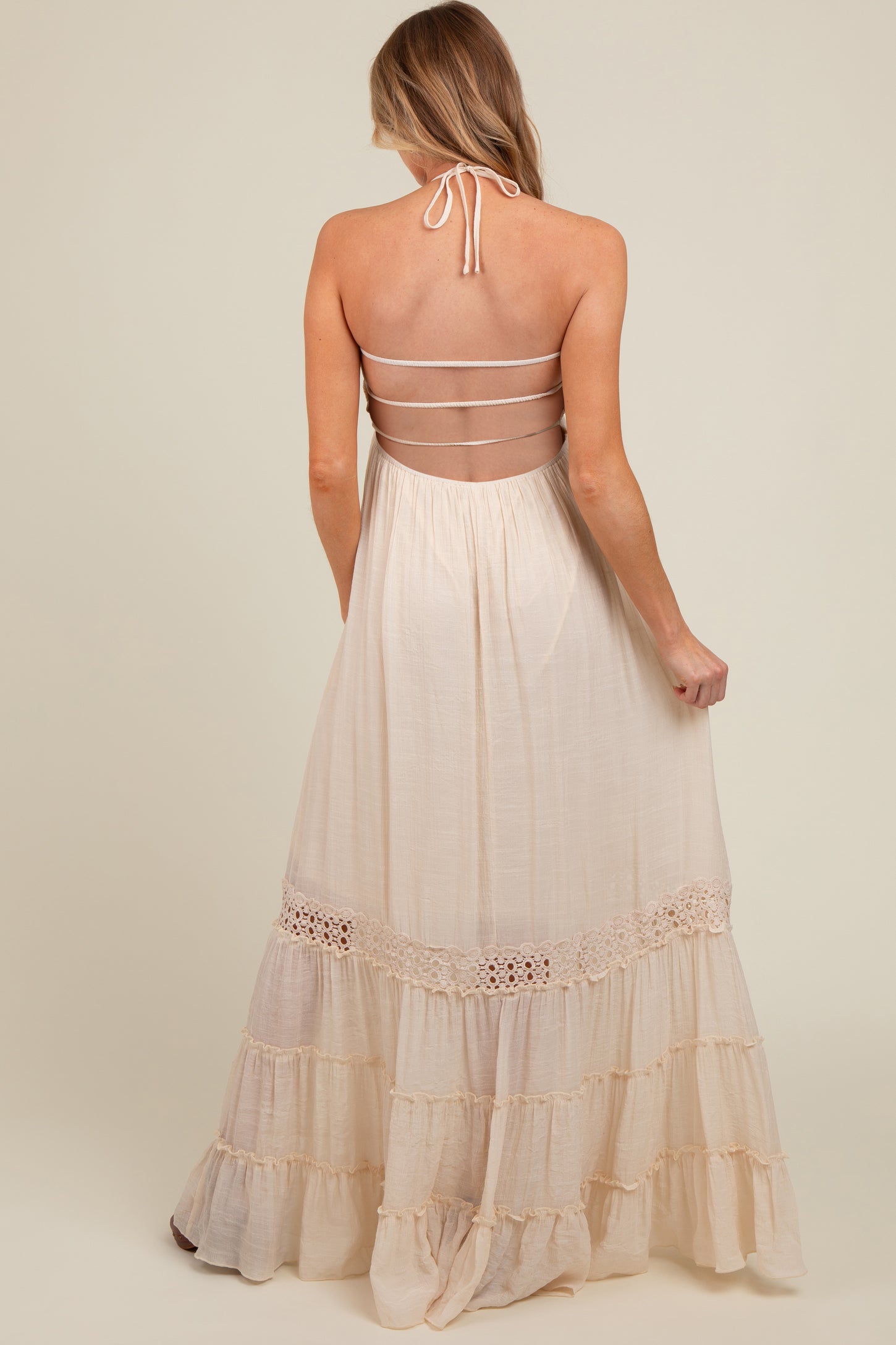 woman wearing a cream-colored maternity maxi dress with a halter neck and tiered ruffle details on the skirt