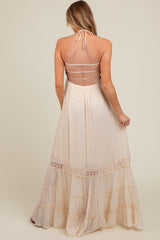 woman wearing a cream-colored maternity maxi dress with a halter neck and tiered ruffle details on the skirt