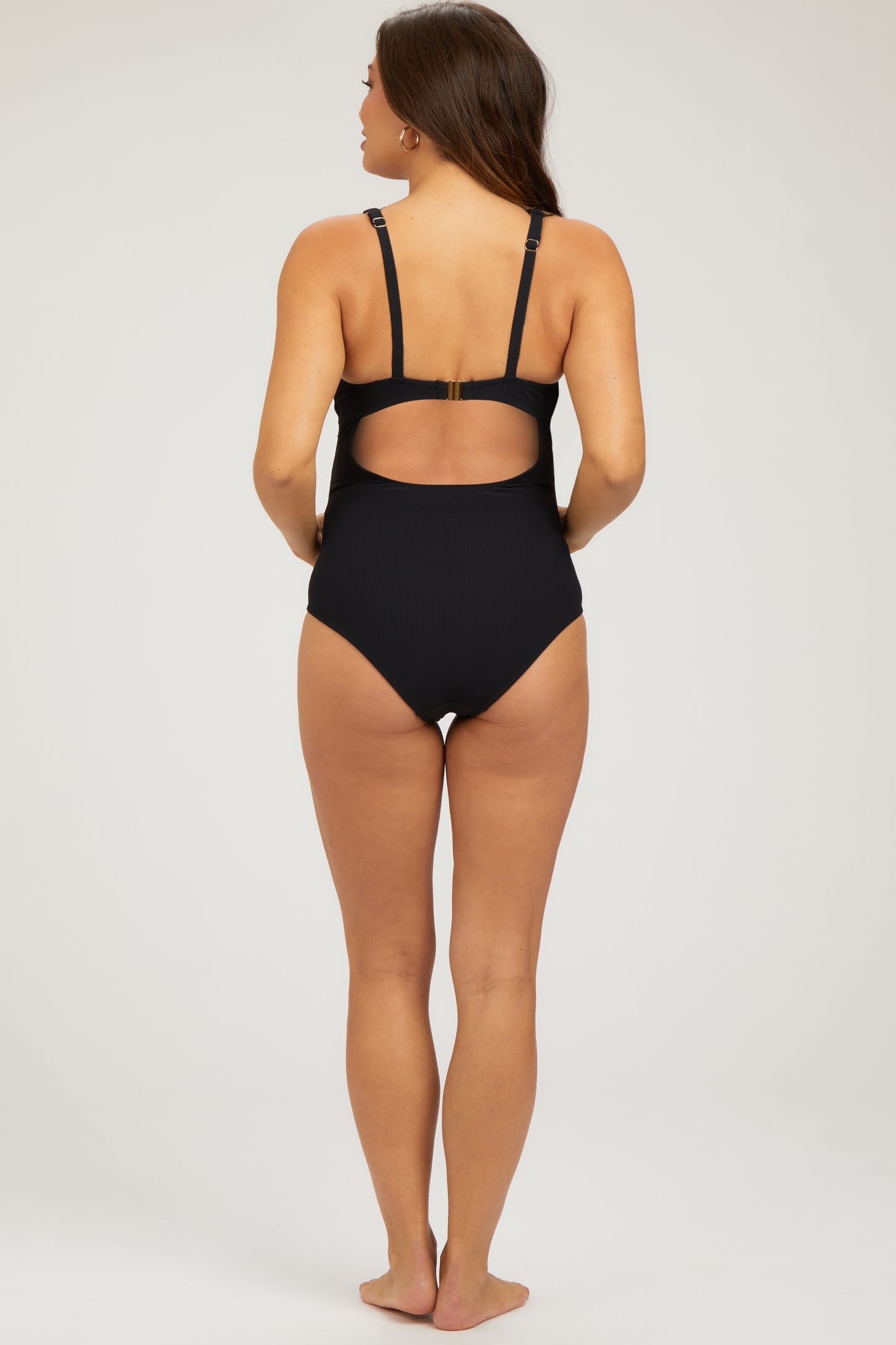 woman wearing a black maternity swimsuit with a cutout back and adjustable straps, showing a baby bump