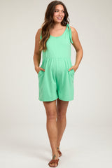 woman wearing a mint green maternity romper with pockets and a tie detail on the shoulder
