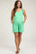 woman wearing a mint green maternity romper with pockets and a tie detail on the shoulder