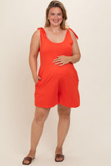 woman wearing a bright orange maternity plus romper with tie straps and pockets, holding her baby bump