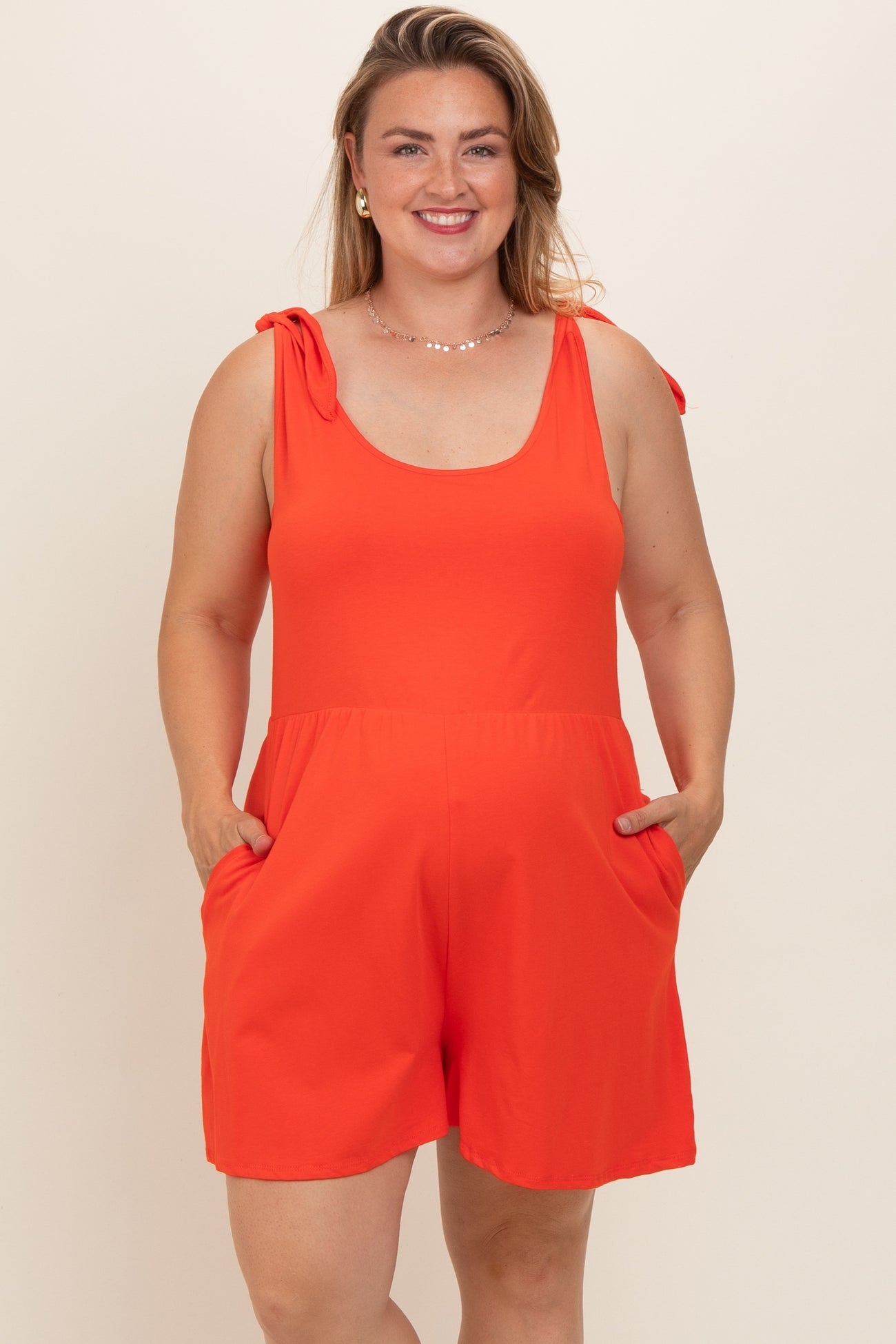 woman wearing a bright orange maternity plus romper with bow tie straps and pockets