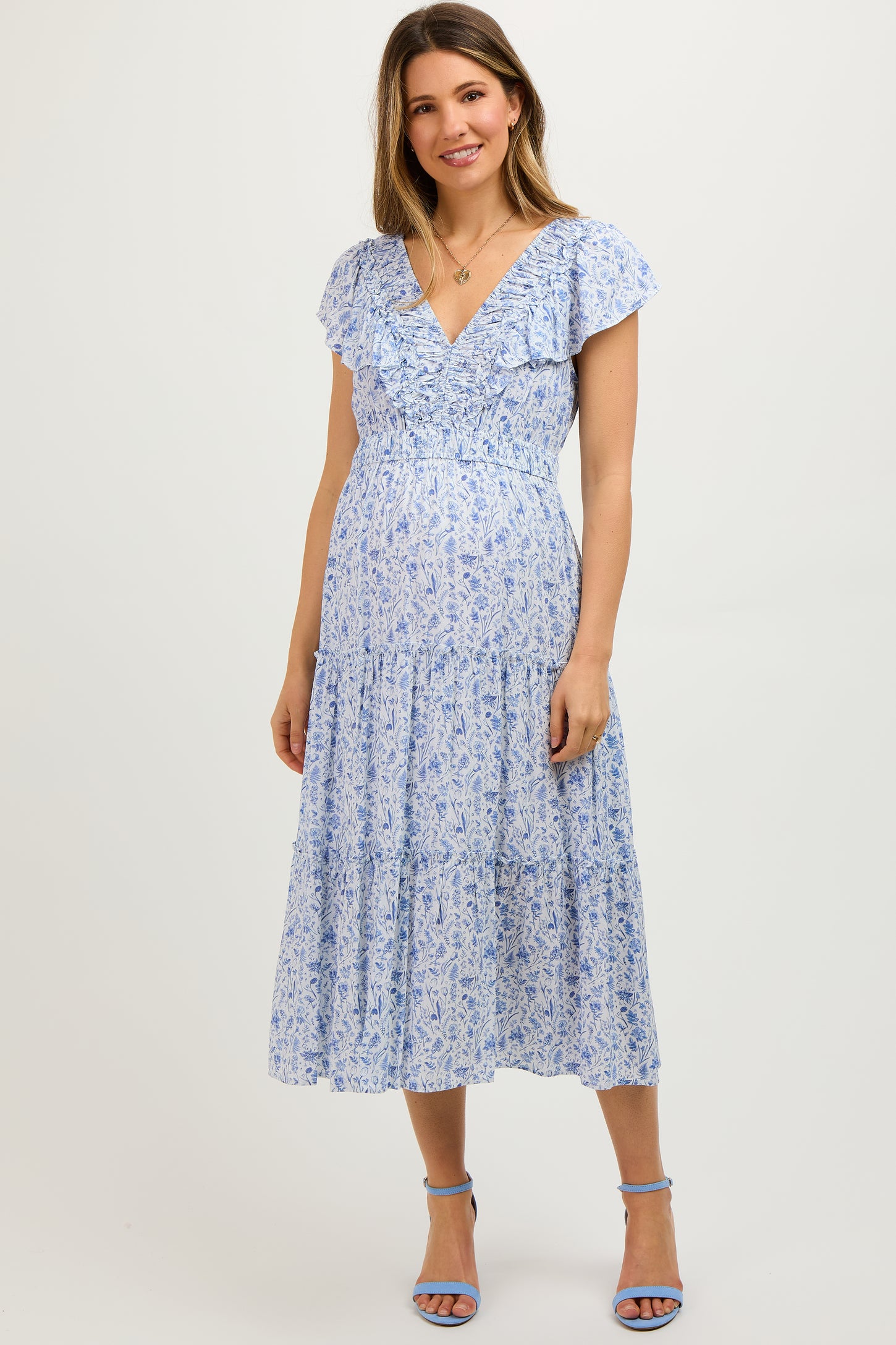 woman wearing a light blue floral maternity dress with ruffled sleeves and a tiered skirt, showing her baby bump