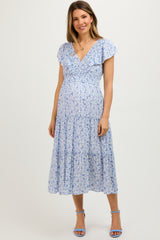 woman wearing a light blue floral maternity dress with ruffled sleeves and a tiered skirt, showing her baby bump