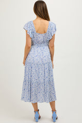 woman wearing a light blue floral maternity dress with ruffled sleeves and a flowing skirt, showing a baby bump