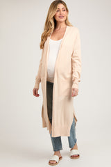 woman wearing a light peach maternity cardigan over a white top and jeans, showing her baby bump