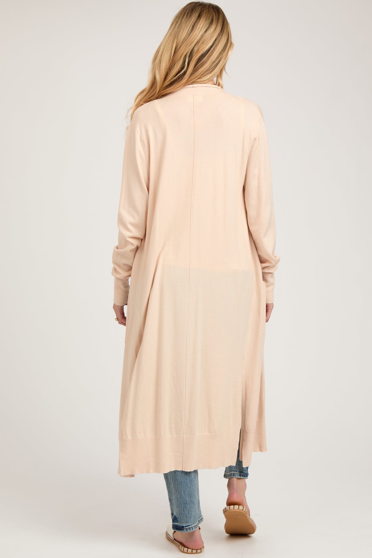 woman wearing a light pink long cardigan with a flowy design, styled over blue jeans