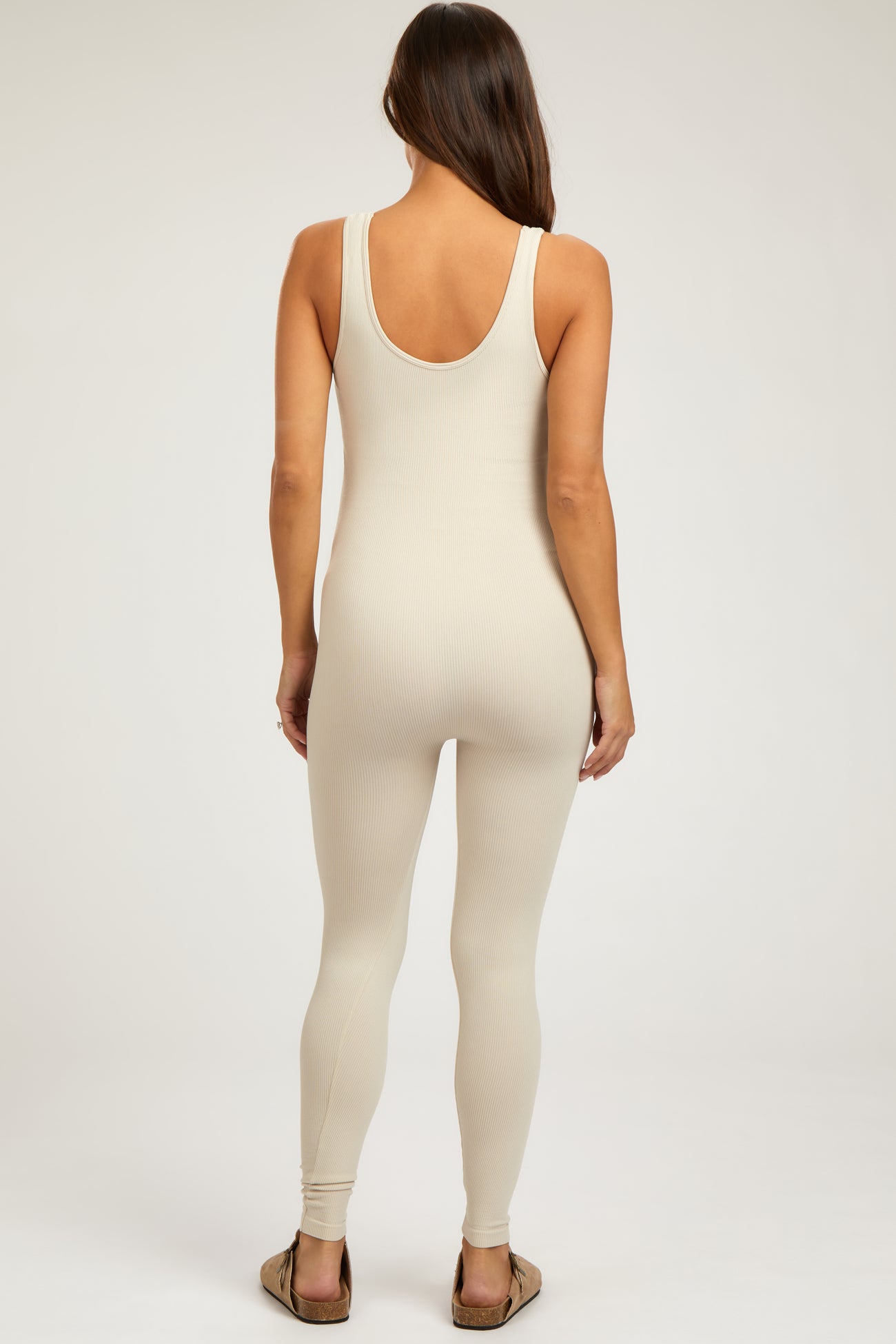 woman wearing a beige ribbed maternity jumpsuit with a scoop back and form-fitting design