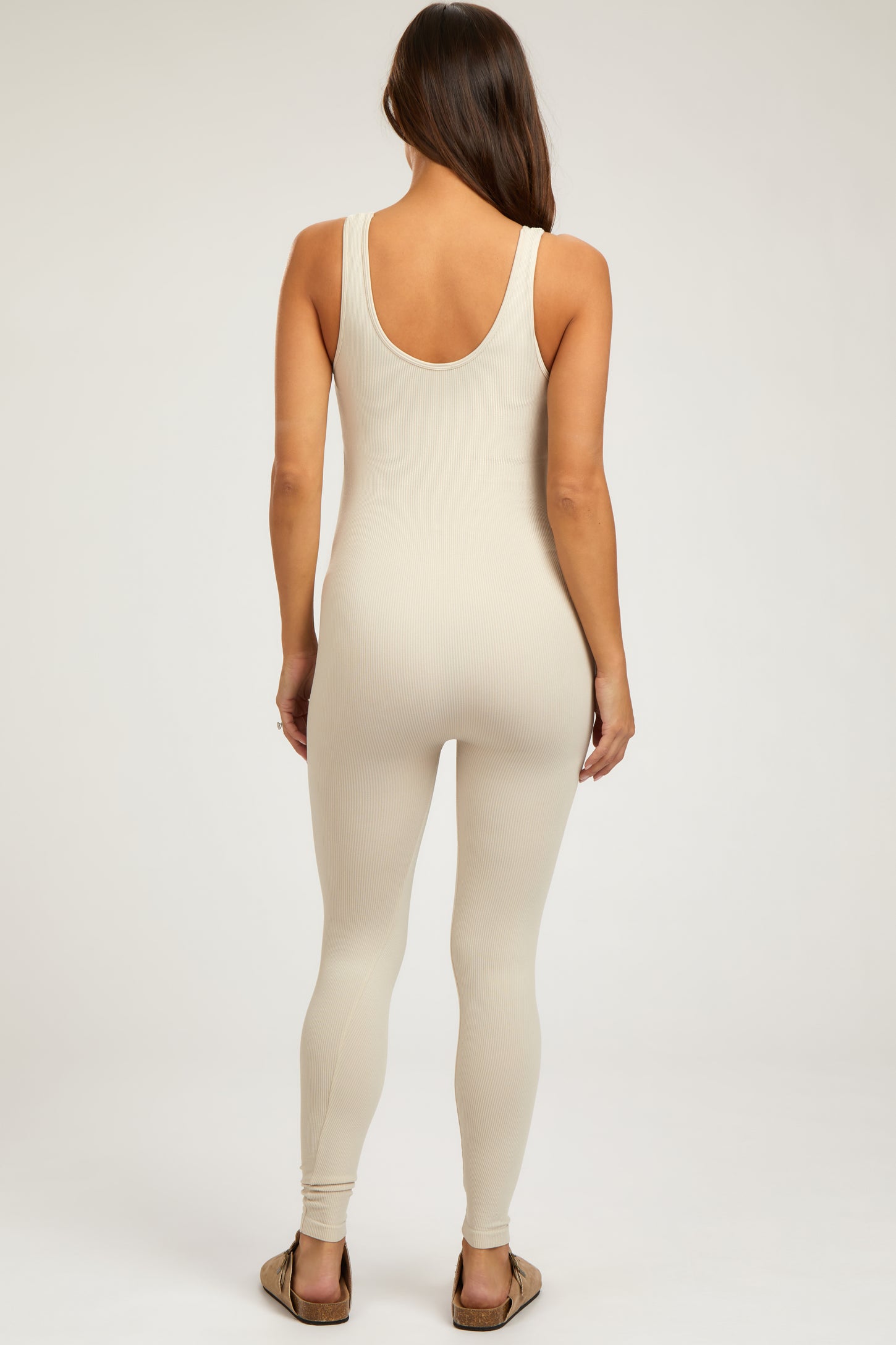 woman wearing a beige ribbed maternity jumpsuit with a scoop back and form-fitting design