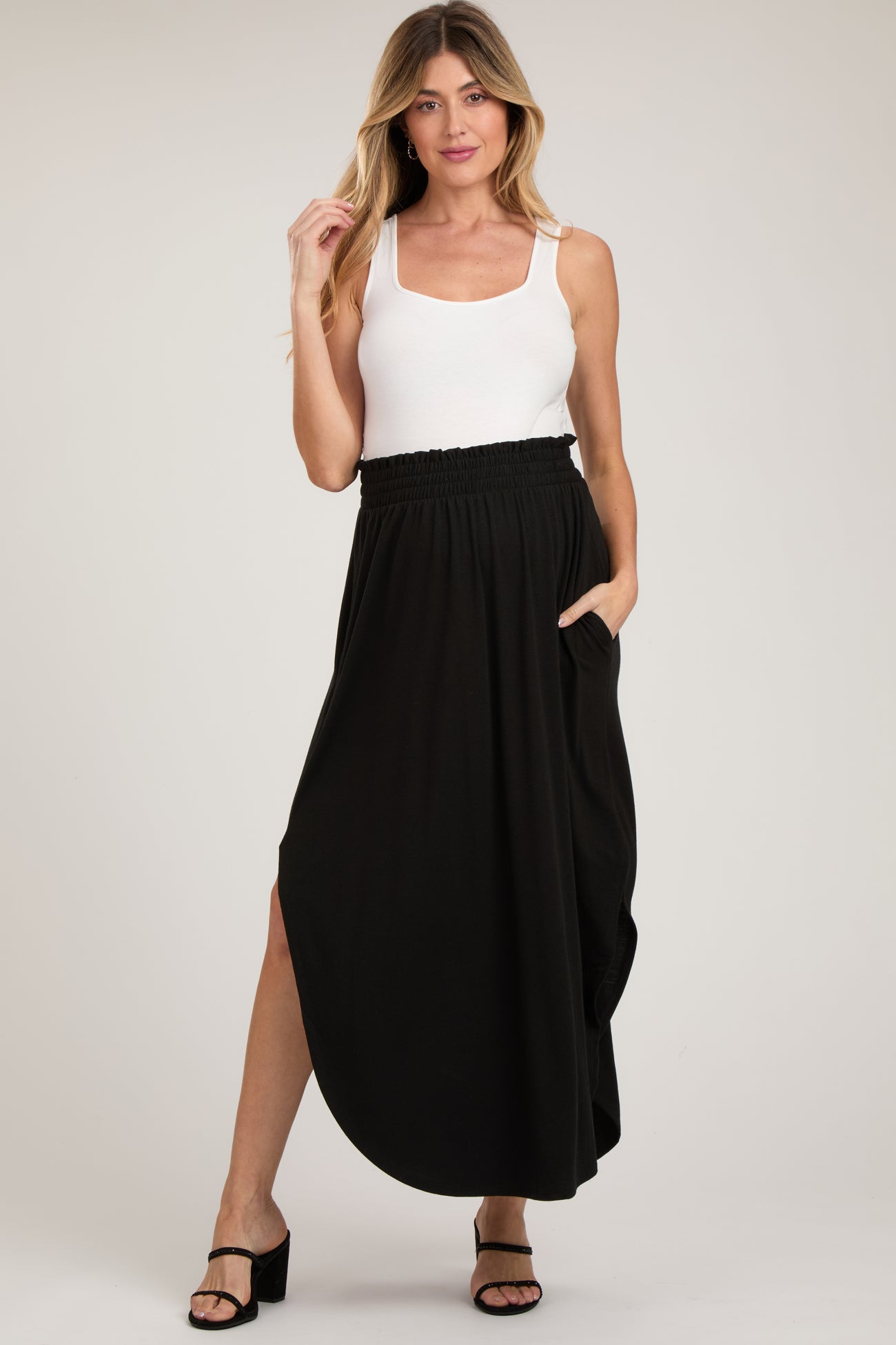 woman wearing a black maternity maxi skirt with pockets and a side slit, paired with a white tank top