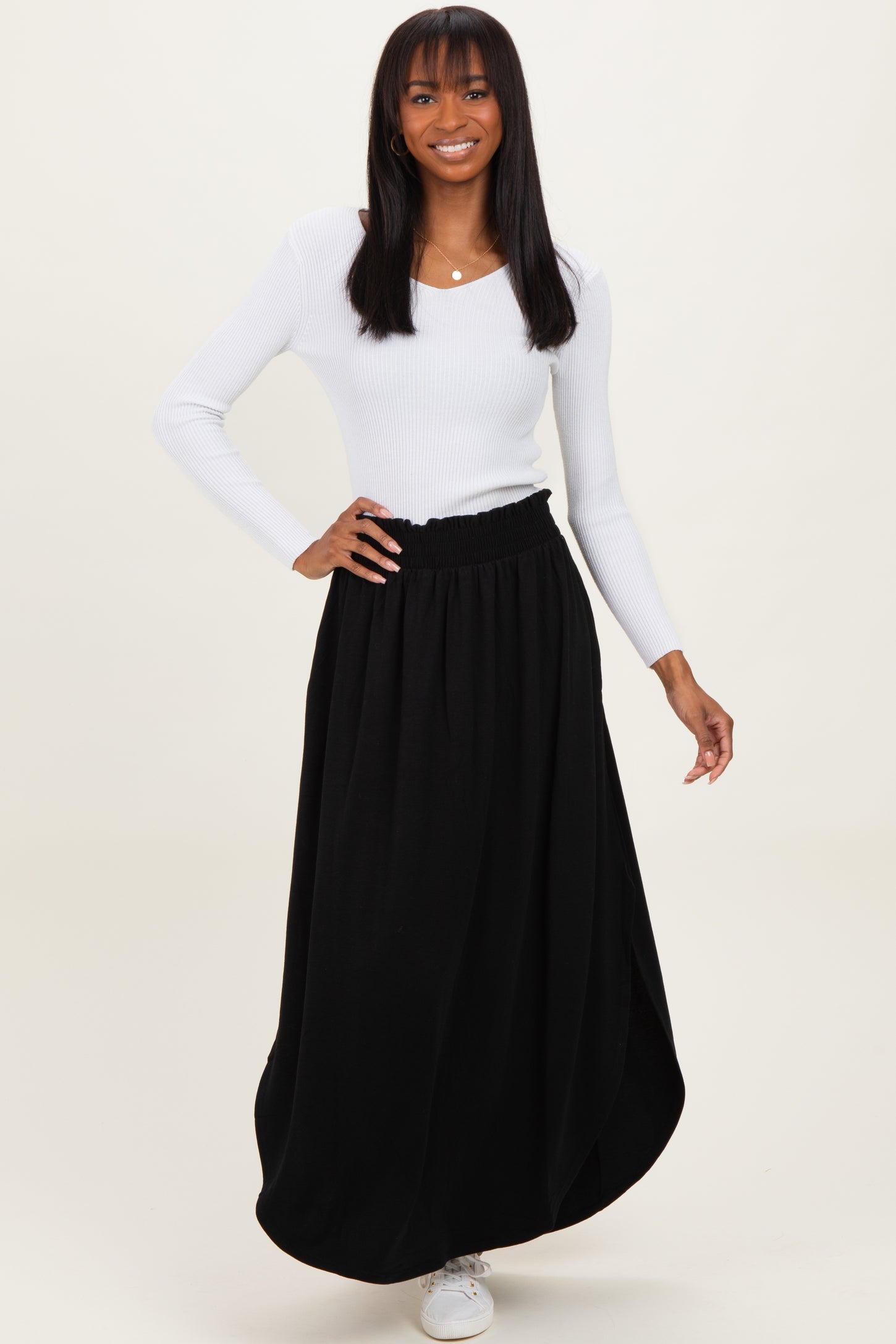 woman wearing a white long sleeve ribbed top and a black maxi skirt, posing with a smile