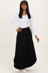 woman wearing a white long sleeve ribbed top and a black maxi skirt, posing with a smile