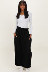 woman wearing a white ribbed long sleeve top and a black maxi skirt with pockets, standing against a neutral background