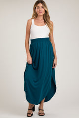 woman wearing a teal maternity maxi skirt with an elastic waistband and side slits, paired with a white tank top