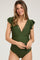 woman wearing an olive green maternity swimsuit with ruffled sleeves and a plunging neckline, holding her baby bump