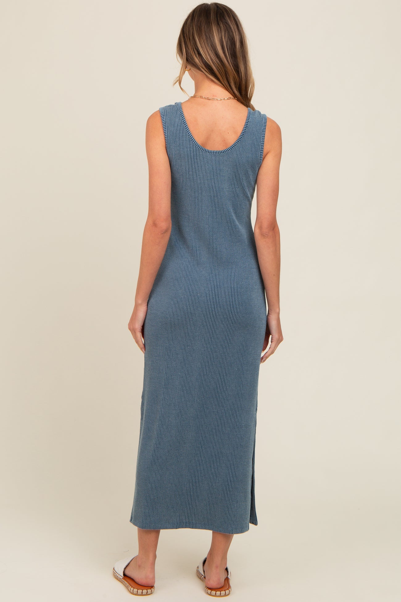 woman wearing a fitted blue ribbed maxi dress with a scoop neckline and side slits, viewed from the back